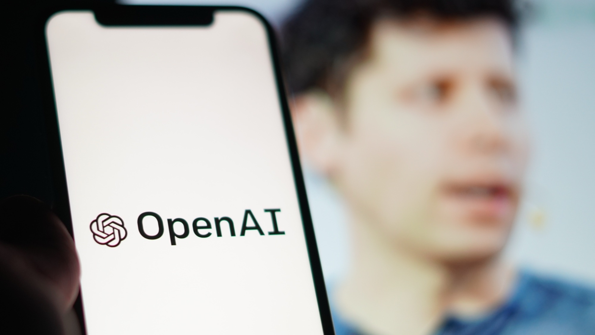 一部手机上写着“OpenAI”，后面跟着Sam Altman。
