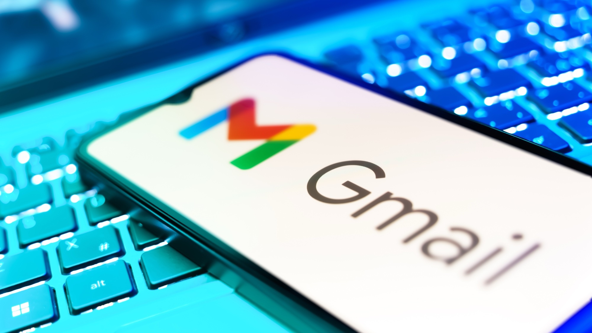 一部带有 Gmail 标志的智能手机放在电脑键盘上。