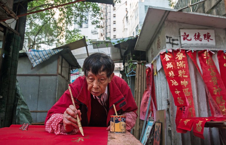 在中国香港的一个市场摊位上，一名中国男子正在用红色装饰品书写中国书法，庆祝农历新年。